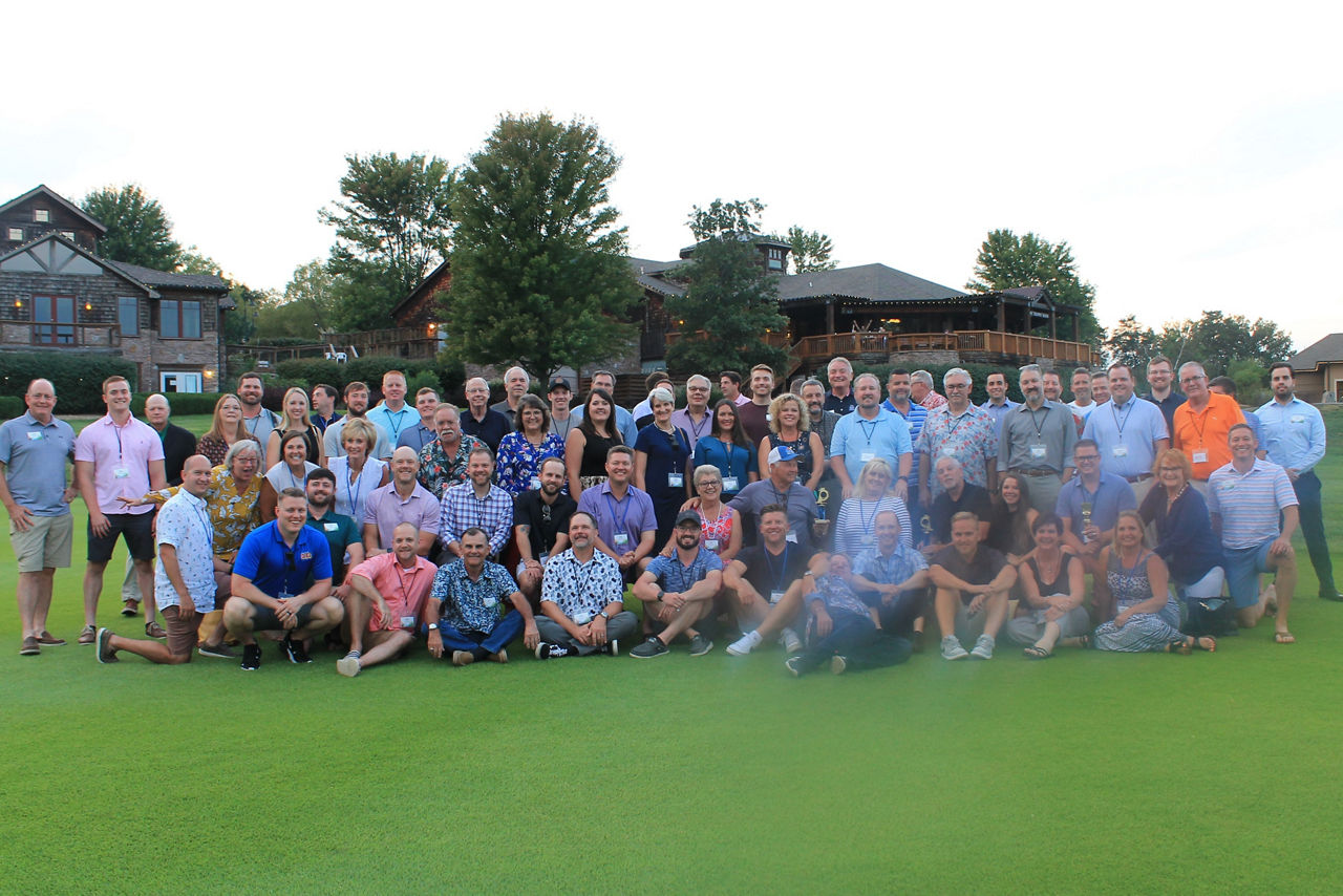 Group photo of approximately 50 symposium attendees outdoors on the grass.